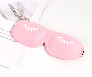 Detailed view of a pink 3D sleep mask with eyelash print on a minimalist white desk
