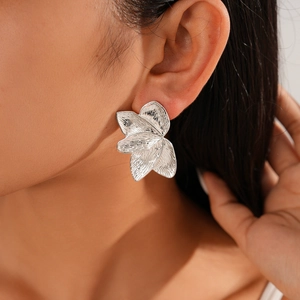 Macro detail of silver petal earrings with brushed metallic texture worn by a model