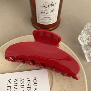 Detail of a large glossy red acetate hair claw clip on a ceramic tray in an aesthetic setting