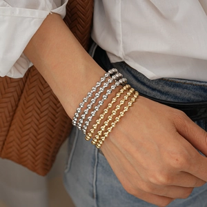 Primo piano di bracciali a strati con perle di metallo oro e argento sul polso