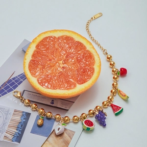 Detail shot of a gold charm bracelet with enamel fruit pendants like cherry and pineapple