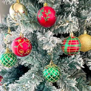 Detailed view of red and green painted Christmas ball ornaments hanging on a snowy tree branch