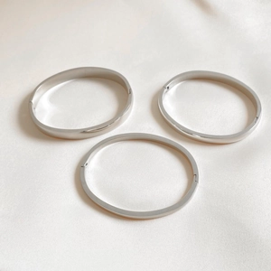Three minimalist polished silver stainless steel bangles with secure clasp on white silk