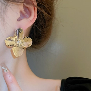 Close-up of oversized gold flower stud earrings with zircon inlay worn by a model