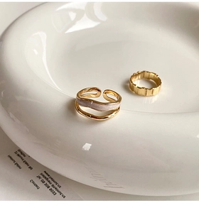 Detail of double-layer pink enamel ring and wavy gold band in a ceramic tray