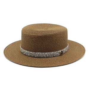 Detailed view of the sparkling rhinestone band and golden M-logo on a straw boater hat