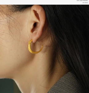 Macro shot of gold-plated crescent earrings with textured hammering on a model's ear