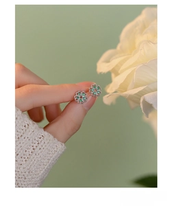 Macro detail of S925 silver flower stud earring with green zircon on fingertip