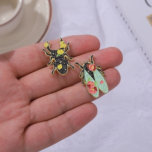 Handheld view of enamel beetle and moth brooch set with floral and geometric patterns