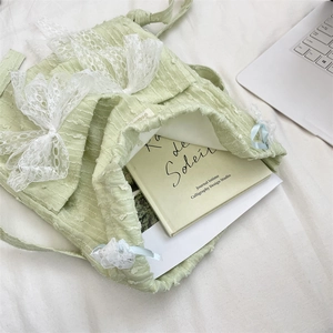 Detail of light green floral lace backpack with ribbons and books inside on a white bed