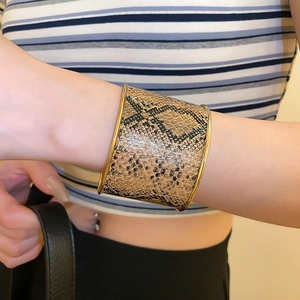 Wide cuff bracelet with snake skin pattern and gold edges on a model's wrist