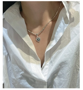 Close-up of heart-shaped silver pendant with lettering worn on a white shirt