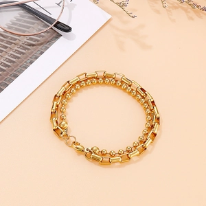 Detail of gold double-layer bracelet with bead and geometric box chains on warm beige background