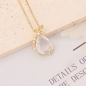 Macro view of a gold angel pendant with a clear teardrop crystal on a fine link chain