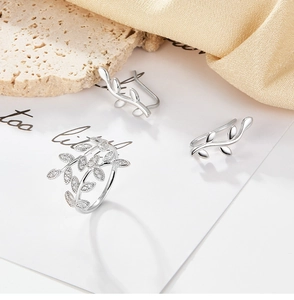 Macro detail of silver leaf rings and ear cuffs with diamonds on elegant satin backdrop