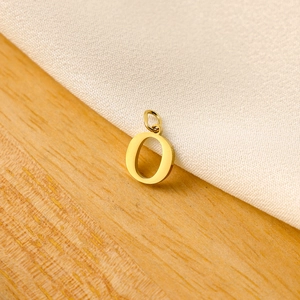 Macro shot of a polished gold letter O charm pendant on white fabric background