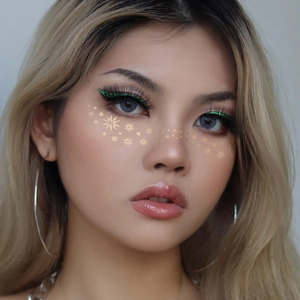 Golden foil star face stickers and green glitter eyeliner on a female makeup model