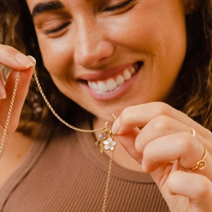 Gold necklace with square purple zircon and white four-leaf clover charm on a model