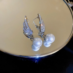 Close-up of silver wing earrings with sparkling rhinestones and elegant white pearls