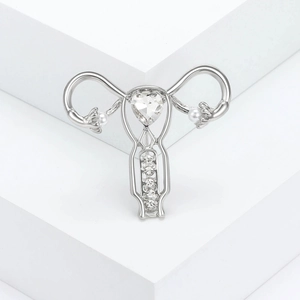 Silver stylized uterus brooch with heart crystal and white imitation pearls on a stand
