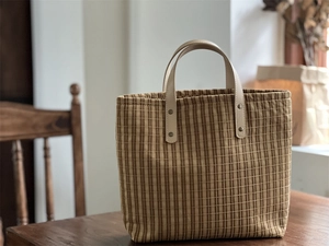 Detail of vintage plaid canvas tote with leather handles and metallic rivet fasteners