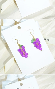 Close-up of purple grape earrings with gold hooks and green leaves on satin background