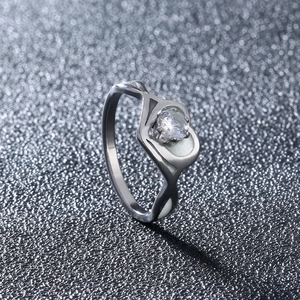 Close-up of silver hollow heart ring with luminous zircon on gray textured surface