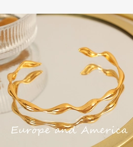 Detailed view of a gold wavy bangle with polished mirror finish on reflective surface
