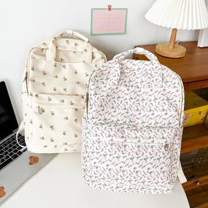Detail of two floral print backpacks in beige and white on a minimalist desk setup