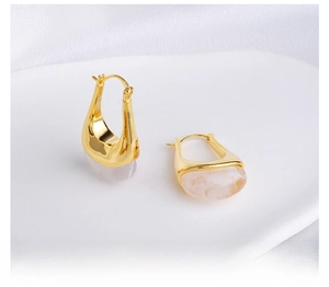 Detail of gold U-shaped earrings with white marbled resin pendants on a tray