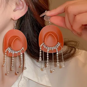 Matte orange cowboy hat earrings with silver rhinestone fringe tassels on a model