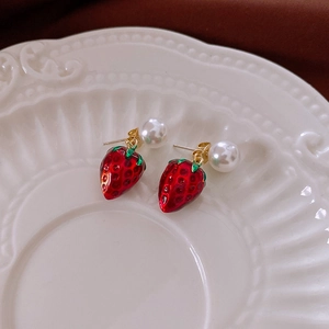 Detailed close-up of glossy red strawberry earrings with pearls on a ceramic tray