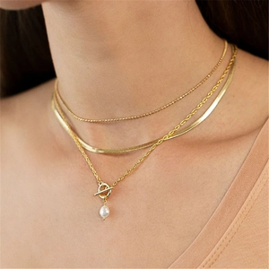 Detailed view of triple-layered gold necklaces with pearl pendant on model neck