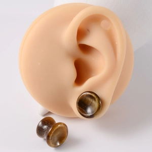 Macro detail of natural tiger eye stone ear plugs on a silicone model ear display