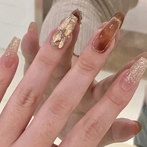 Detail of long ballerina nails featuring amber texture with gold glitter and 3D shell accents