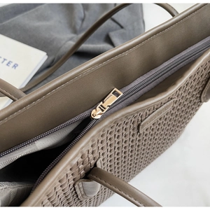 Close-up of brown woven texture tote bag featuring a gold zipper and sturdy handle detail