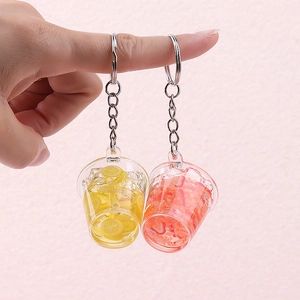 Miniature juice cup keychains with lemon and strawberry slices on a pink background