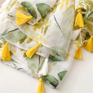 Detail of yellow and green leaf print on cotton scarf with colorful fringed tassels