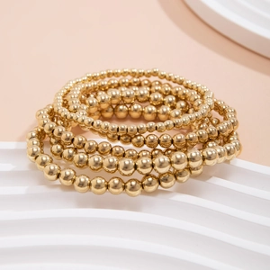 Detail of five-piece gold beaded bracelet set with heart pendant on white display stand