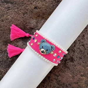 Close-up of handmade woven pink bracelet featuring blue rhinestone bear and pearl trim