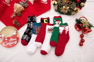 Flat lay of colorful Christmas coral fleece socks with festive ornaments on white fabric
