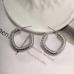 Close-up of silver C-shaped hoop earrings with twisted spiral texture on a white plate