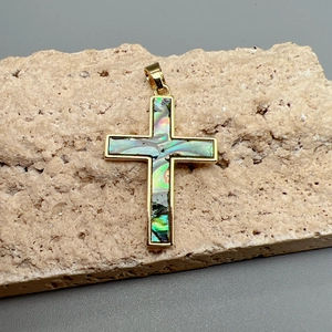 Golden cross pendant with colorful abalone shell inlay displayed on a textured stone