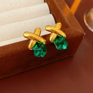 Macro shot of gold cross earrings with emerald green cubic gemstones on a velvet box