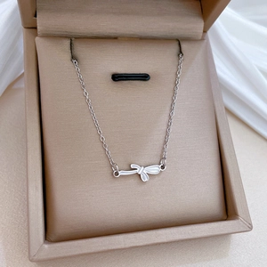 Detailed view of a silver bow necklace in a jewelry box on white silk fabric background