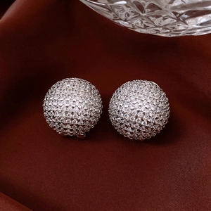 Detail of silver stud earrings with pavé zircons resting on deep red silk fabric