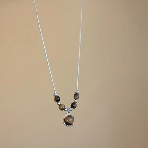 Macro detail of tiger eye stone pendant and silver snake chain with metallic beads