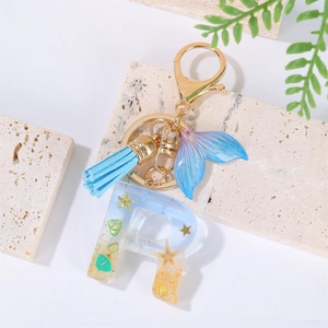 Detail of resin letter R keychain with starfish, blue tassel, and golden ring on stone