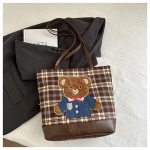 Flat lay of brown plaid canvas tote bag with bear embroidery on white bedding background