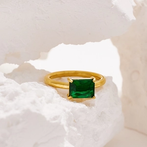 Macro shot of gold-plated ring with a large rectangular emerald stone on a textured rock